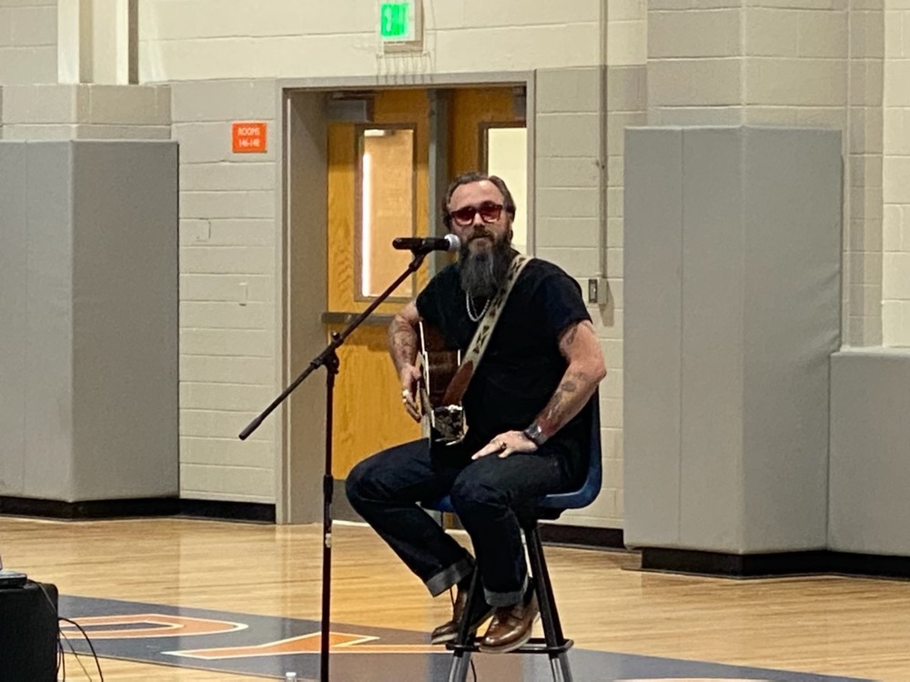 Elvie Shane seated on a stool holding a guitar behind a mic