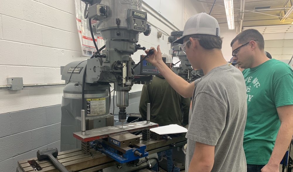Branden Hicks working at a piece of machining equipment as teacher Michael Critchelow looks on
