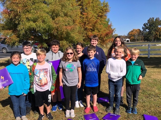 11 male and female Caneyville GT Students on Field Trip outside in front of trees. Some are holding purple folders, standing in two rows.