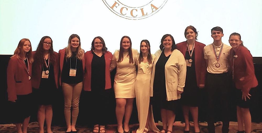 FCCLA State representative students, most in FCCLA red blazers, standing lined up on a stage with sponsor Cody Mooneyhan beneath an FCCLA Logo