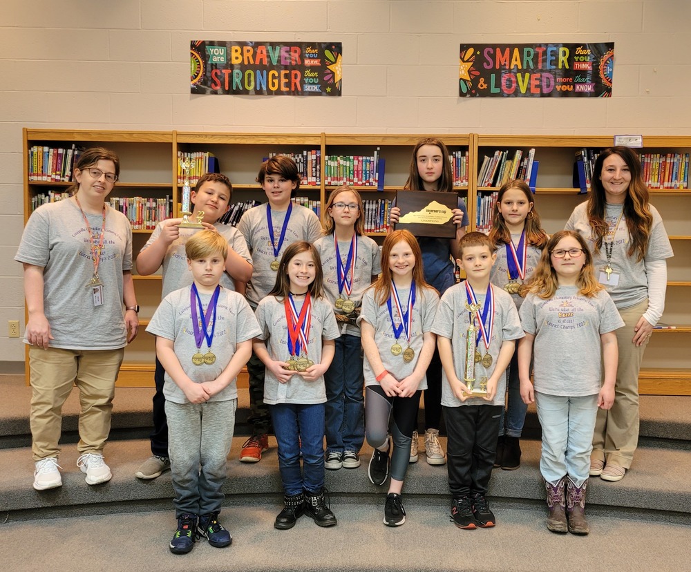 Caneyville Academic Team standing in two rows on library steps back row flanked by sponsors Laura Day and Brittany Smith, shelves of books behind them