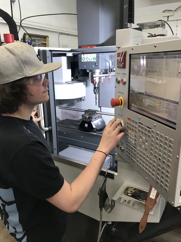 student in a black tee and beige cap programming machining equipment