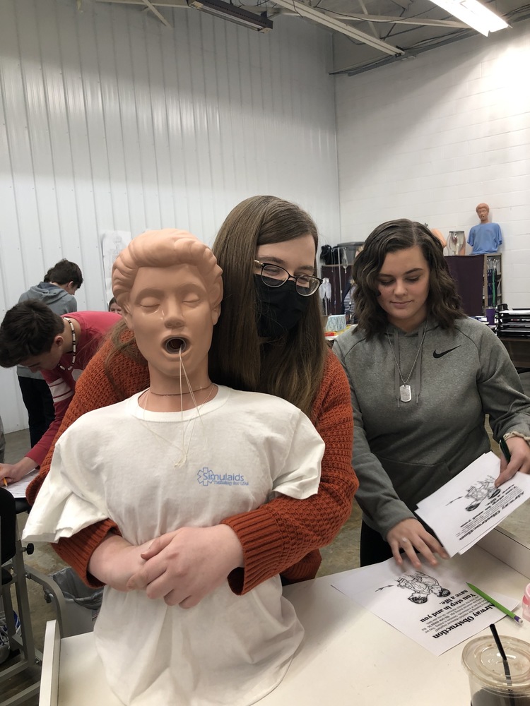 Girl doing mannequin CPR with another looking on  from behind