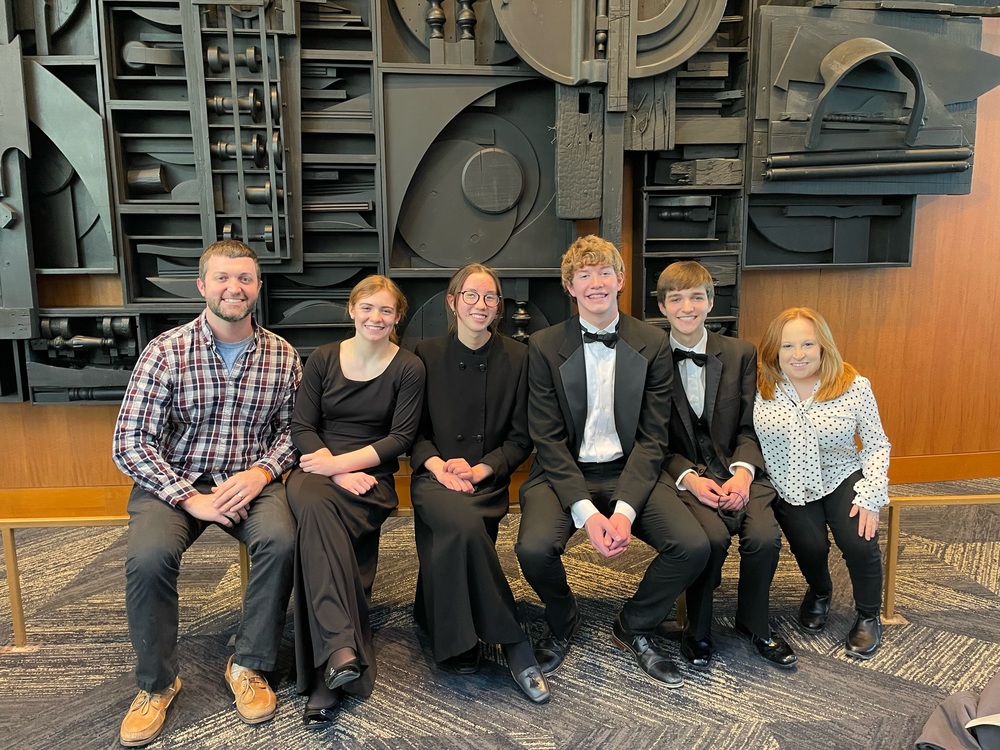 Adam French, Bethany Ray, Michell Lynch, Austin Walker, Dawson Gorby and Stacy French sitting in front of an abstract wall sculpture at All state orchestra, KY Center for the Arts
