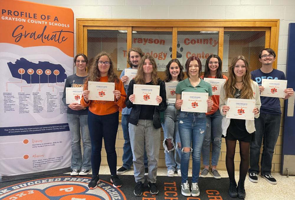 Profile of a GCS Grad vertical banner to left of 7 female and 2 male Tech Center students holding paper certification certificates with orange cougar paw on the middle of them