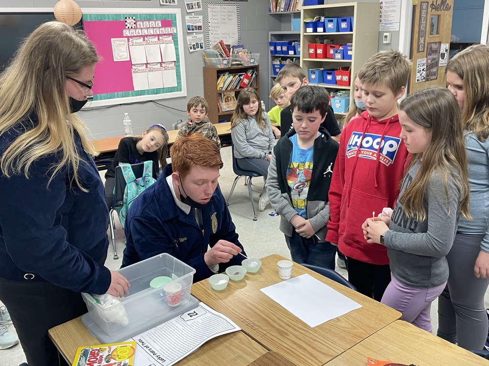 Male and female GCHS students in FFA jackets helping young students with an experiment