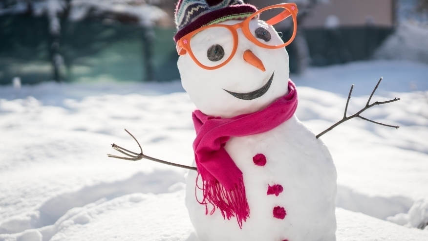 Snowman with twig arms in bright pink scarf and pom buttons with carrot nose, black eyes and smile, carrot nose and orange glasses in striped toboggan
