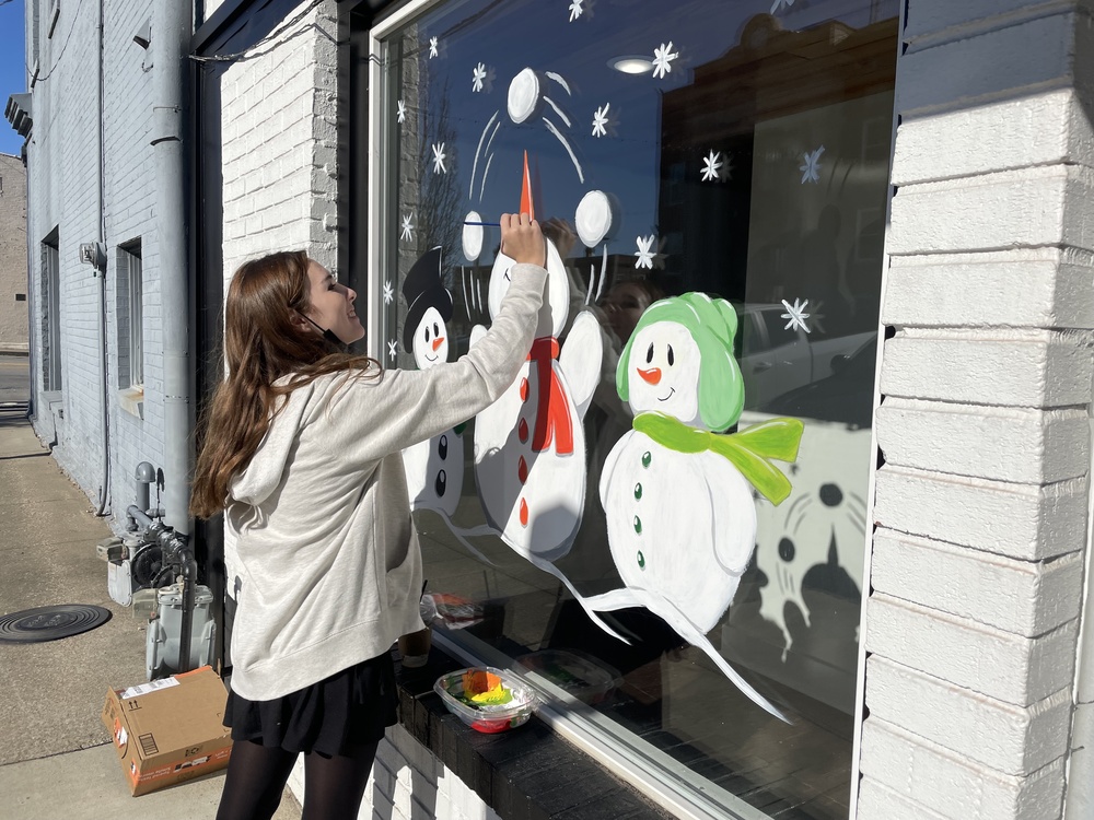 girl painting snowmen on a storefront window