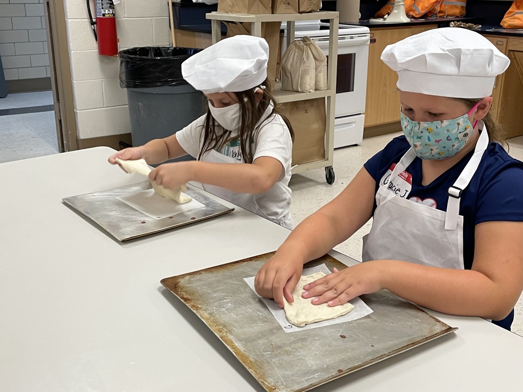 two girls patting dough on trays in chef hats