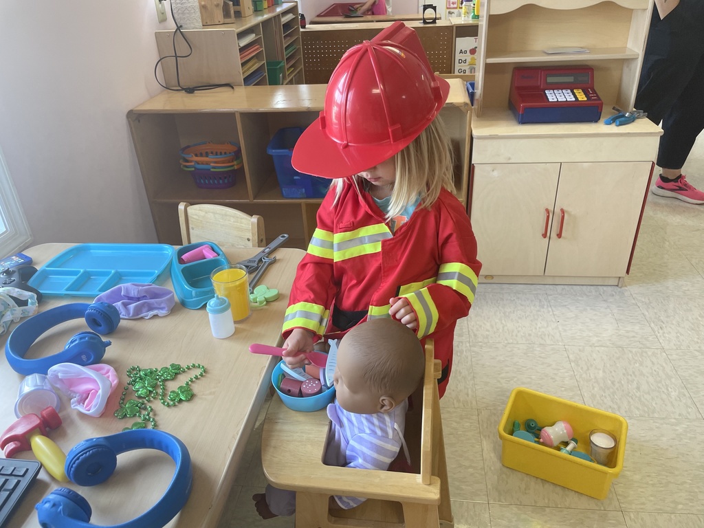 small girl in firemans costume feeding doll in high chair