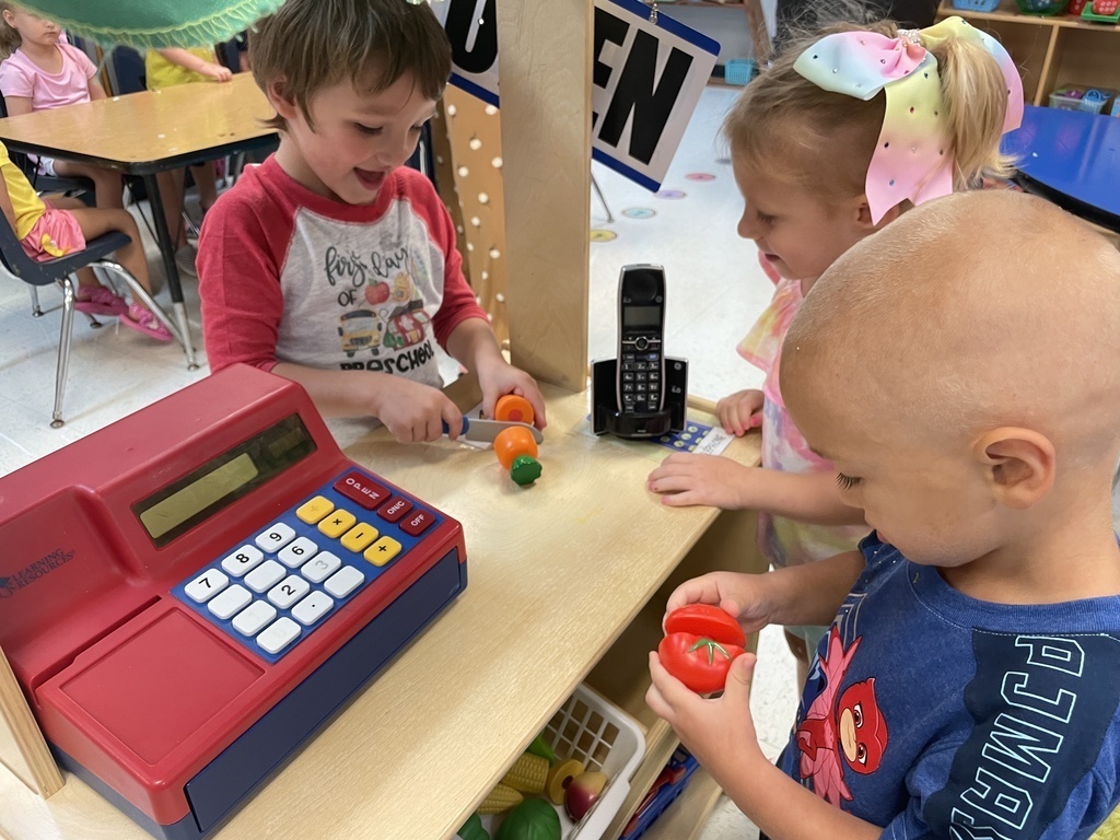 2 small boys and a girl at a toy cahs register with toy vegetables