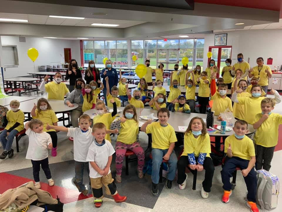 People in yello (and a few white) tshirts celebrating in a lunchroom
