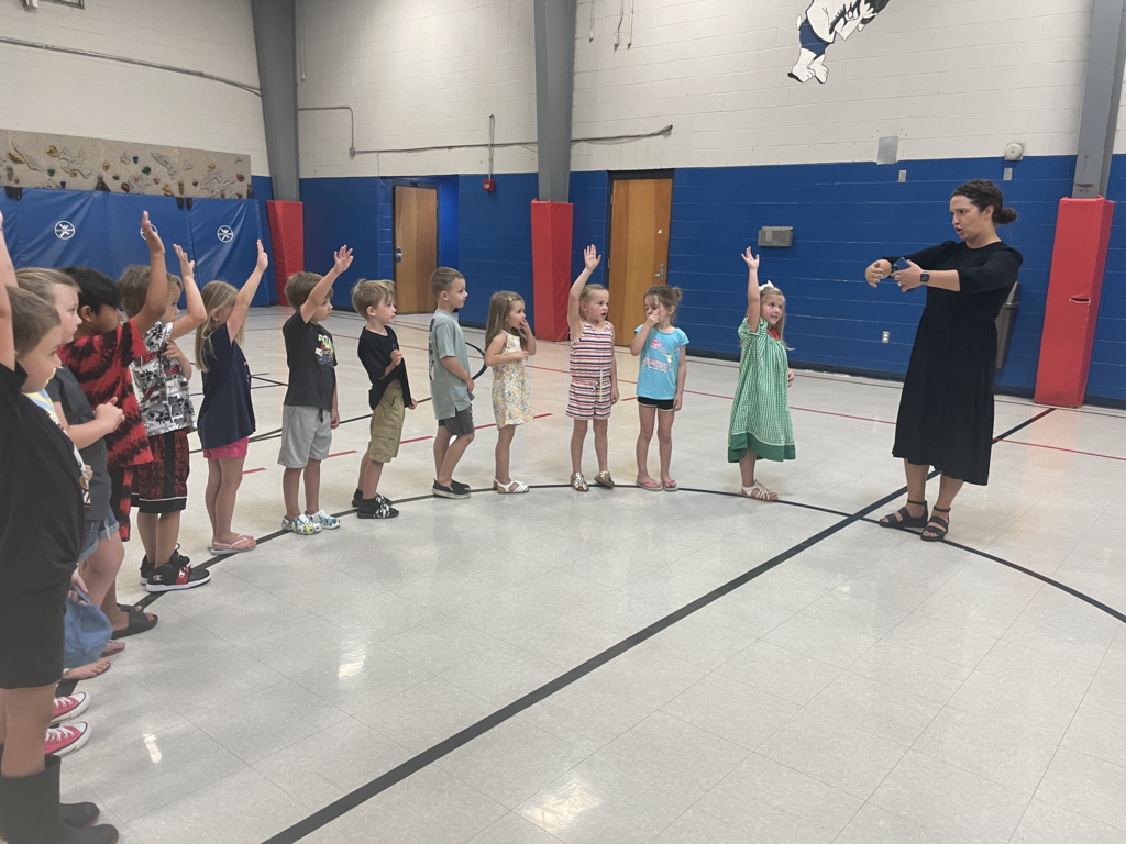 woman in black dress making circle with arms in from of children with arms raised