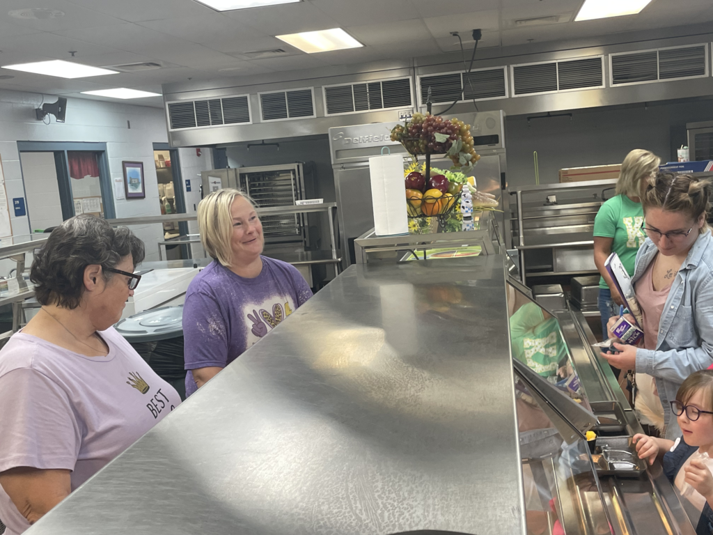 Cafeteria workers talking to parents and children in serving line
