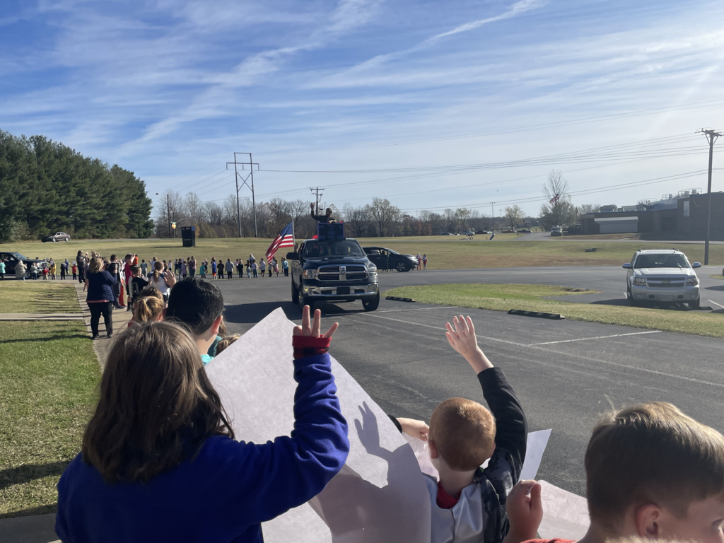 Young children waving to man in truck and holding signs