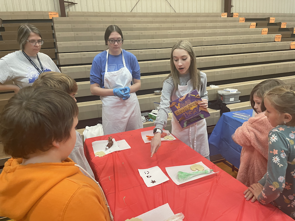 high school girls helping elementary students decorate cookies