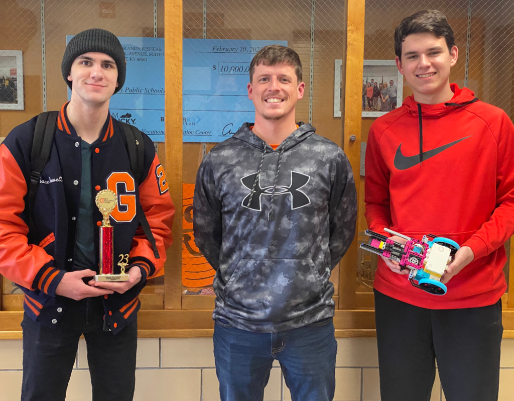 Isaac Dowell holding a trophy, JT Burns, Jake Rogers holding a colorful robot standing in front of a display case.
