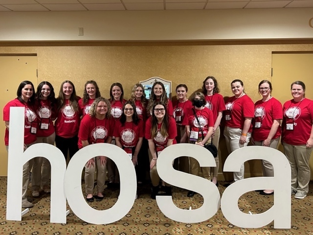 GCHS HOSA members in red t-shirts and khakis standing in rows behind large, white HOSA letters, State Conference 2023